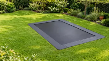 Rektangulær trampolin der ligger helt i niveau med græsplænen, så græsset møder kantpuden, set lidt ovenfra
