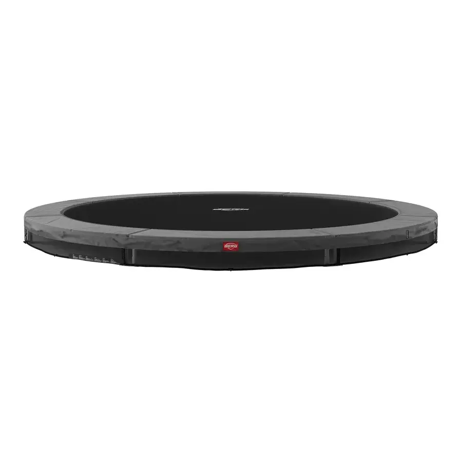 Bred rund BERG Favorit InGround trampolin uden net, grå kantpude og sort dug, set fra siden mod hvid baggrund